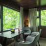 Interior view of a modern tree house with table, chairs and large windows with a view of the greenery.