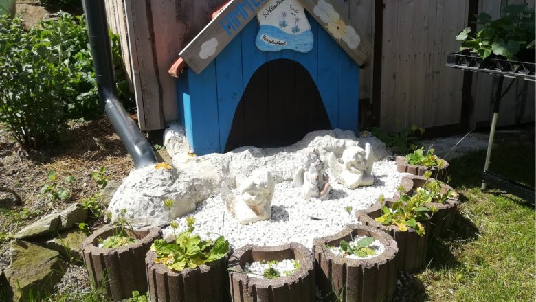 Small blue house with angel figures and plants in a garden.