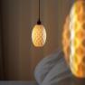 Close-up of a hanging lamp with a honeycomb pattern emitting warm light next to a bed.