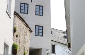 Two people walk along a cobbled alley, past a historic tower with several windows.