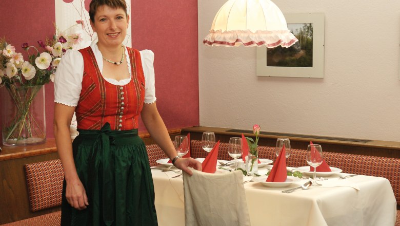 A woman in traditional dress stands next to a laid table in a restaurant.