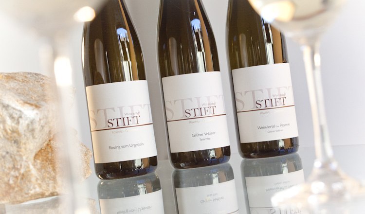 Three wine bottles of the brand Stift on a table, surrounded by wine glasses.