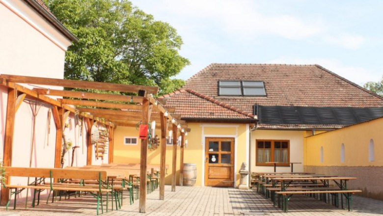 Inner courtyard of a wine bar with wooden benches and tables under a pergola.