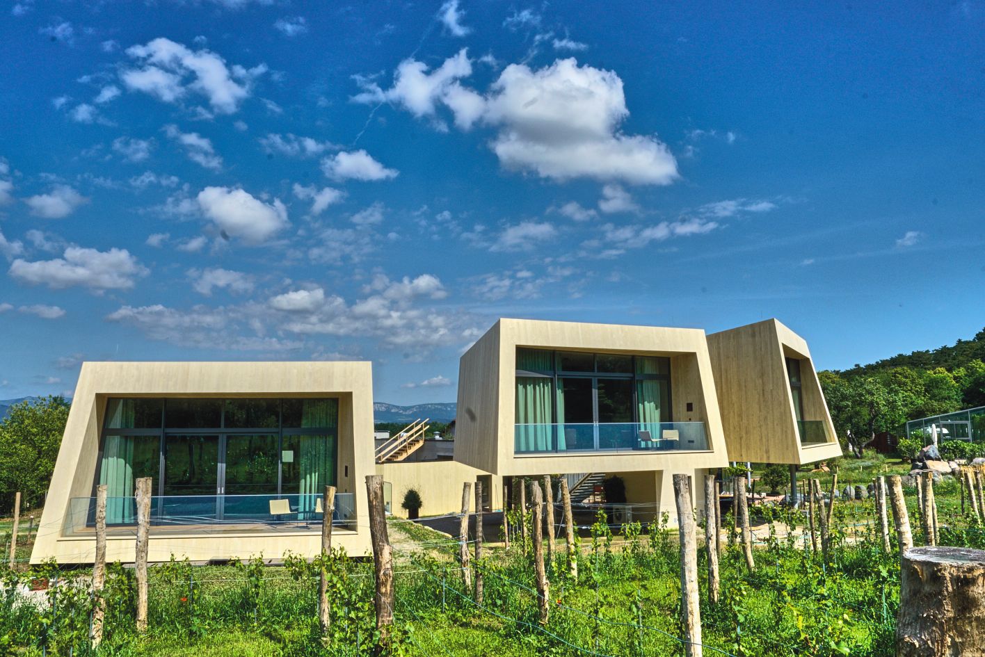 Modern garden lofts with large windows and wood paneling in a green landscape under a blue sky.