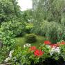 View from the balcony onto a green garden with trees and red and white flowers in the foreground.