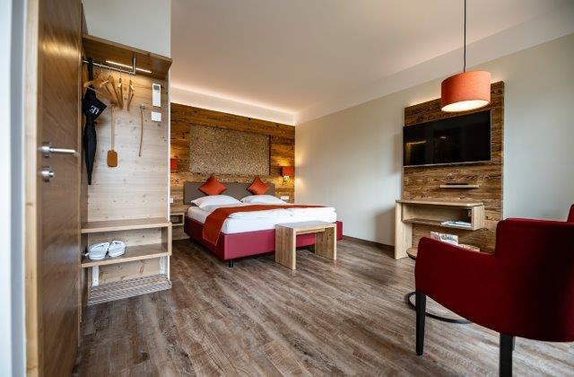 Modern hotel room with double bed, wooden furniture and red armchair.