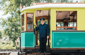 A train driver in uniform stands smiling in the doorway of a historic train.