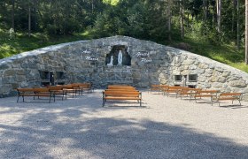 Stone grotto with a statue of the Virgin Mary and benches outside.