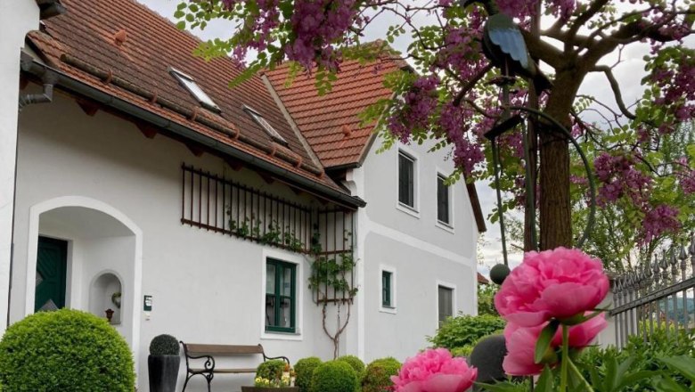 Country house Rossatz, © Familie Schlager A country house with red roof tiles, surrounded by blossoming trees and pink flowers in the foreground.