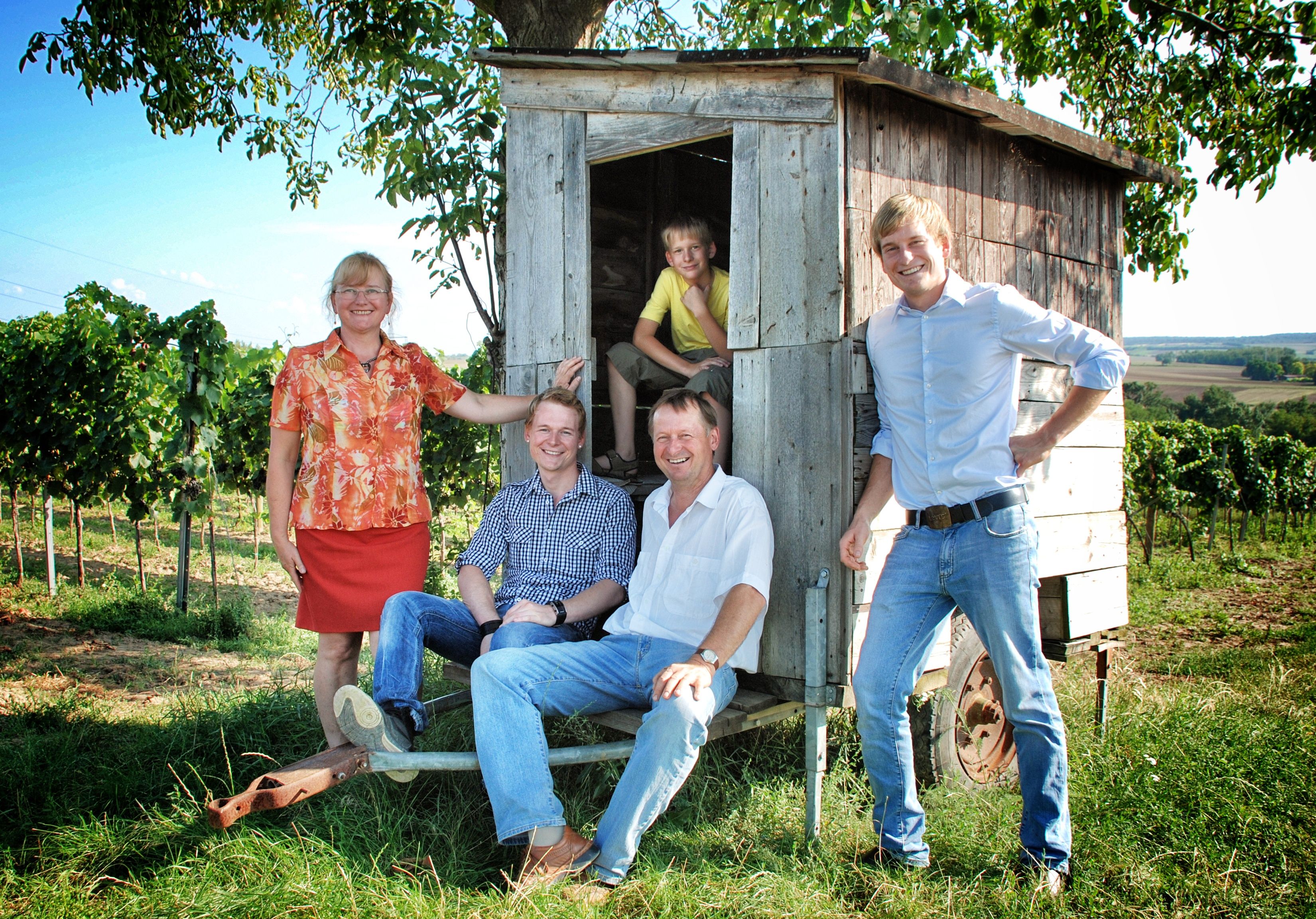 A family poses in front of a small wooden wagon in a vineyard.
