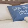 Bed with blue cushion, inscription 'Good Vibes Only'.
