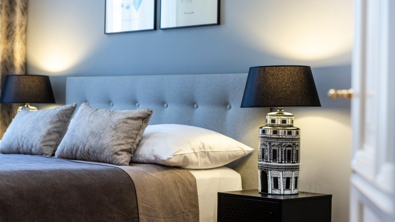 Elegant double room with gray headboard, two pillows, bedside lamp and wall pictures.