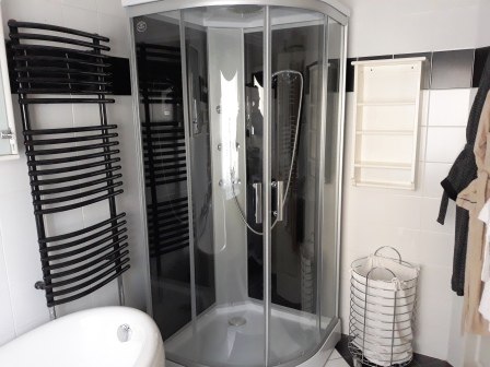 Modern bathroom with shower cubicle, bathtub, towel radiator and laundry basket.