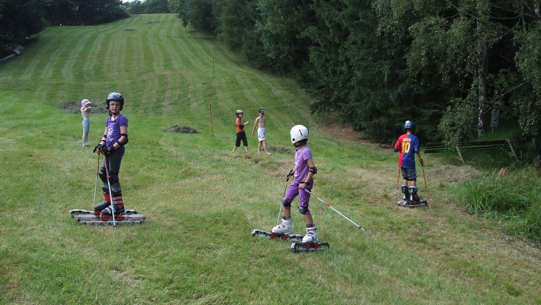 Children skiing with grass skis on a meadow.