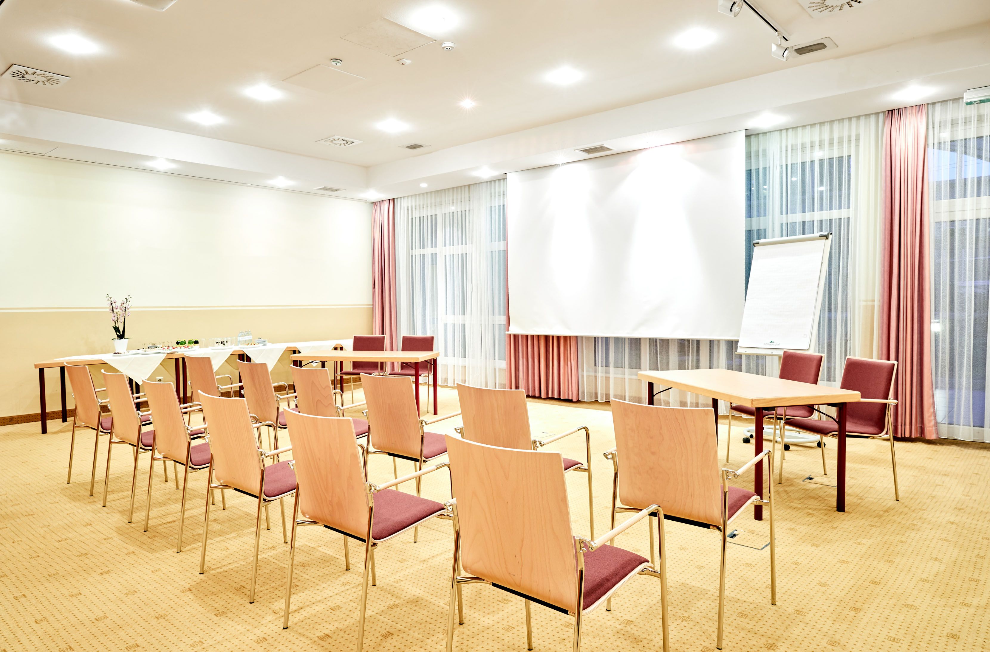 A bright seminar room with chairs, tables, a flipchart and a projection screen.