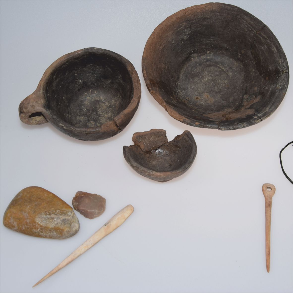 Prehistoric artifacts such as bowls, tools and stones on a white background.