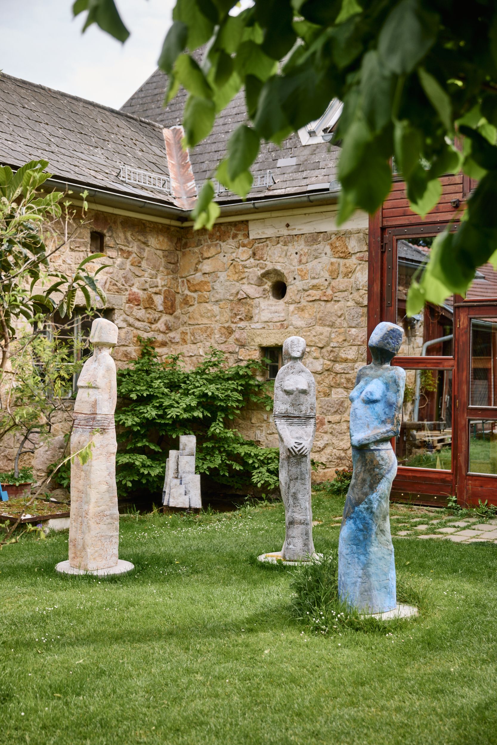 Three colorful sculptures stand on a meadow in front of an old stone building