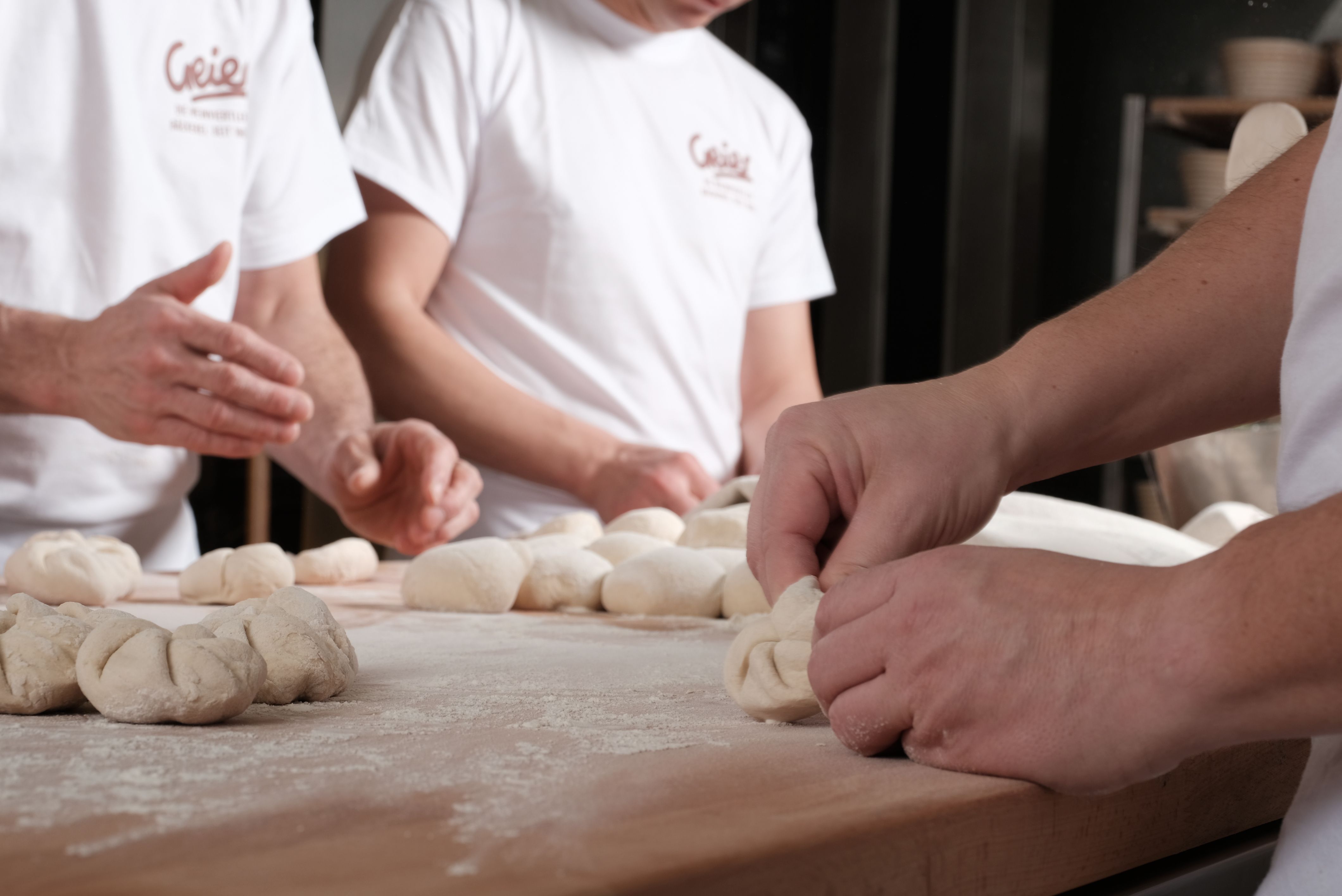 Bakers form dough on a floured table.