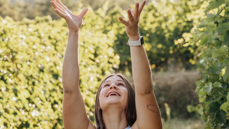 Woman throws wine bottle into the air in a vineyard.