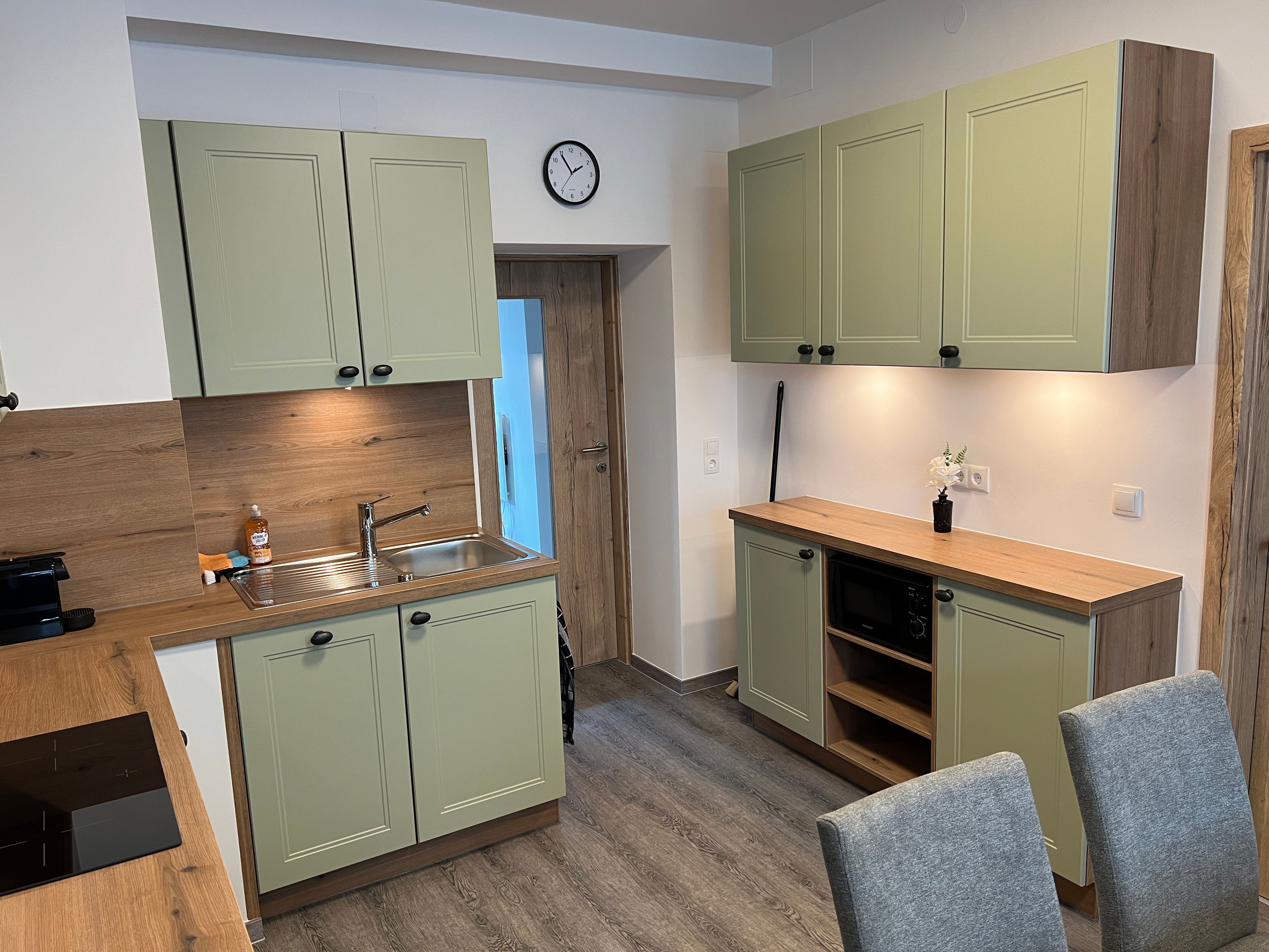 Modern kitchen with green cabinets, wooden worktops and gray chairs.