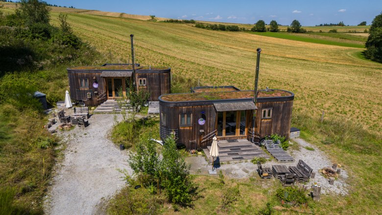 SONNENTOR country lofts, © Niederösterreich Werbung / Maximilian Pawlikowsky Two rustic wooden houses with green roofs in a rural setting.