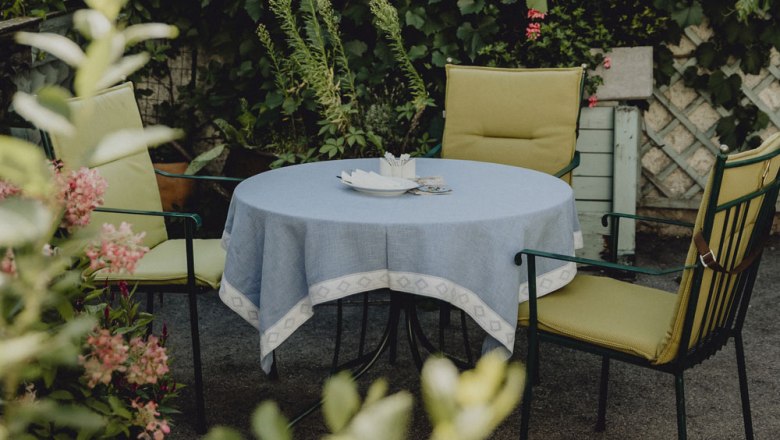 A round table with a blue tablecloth and two green chairs in a garden.