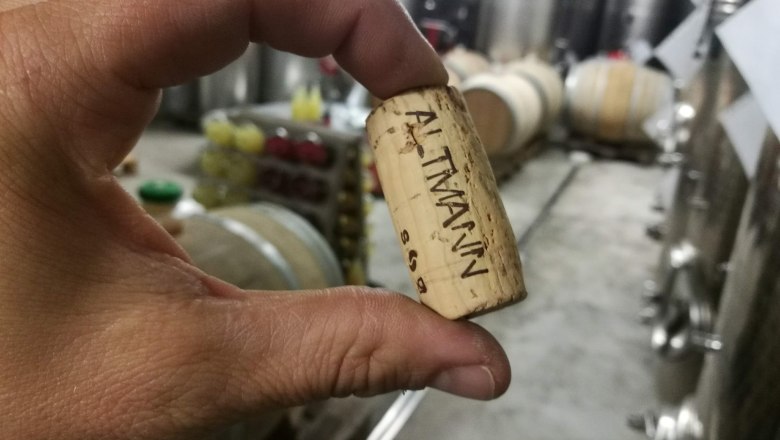Hand holds a wine cork with the inscription 'ALTMANN' in a wine cellar.