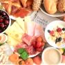 A rich breakfast with cheese, ham, croissants, fruit, muesli, egg and coffee on a table.