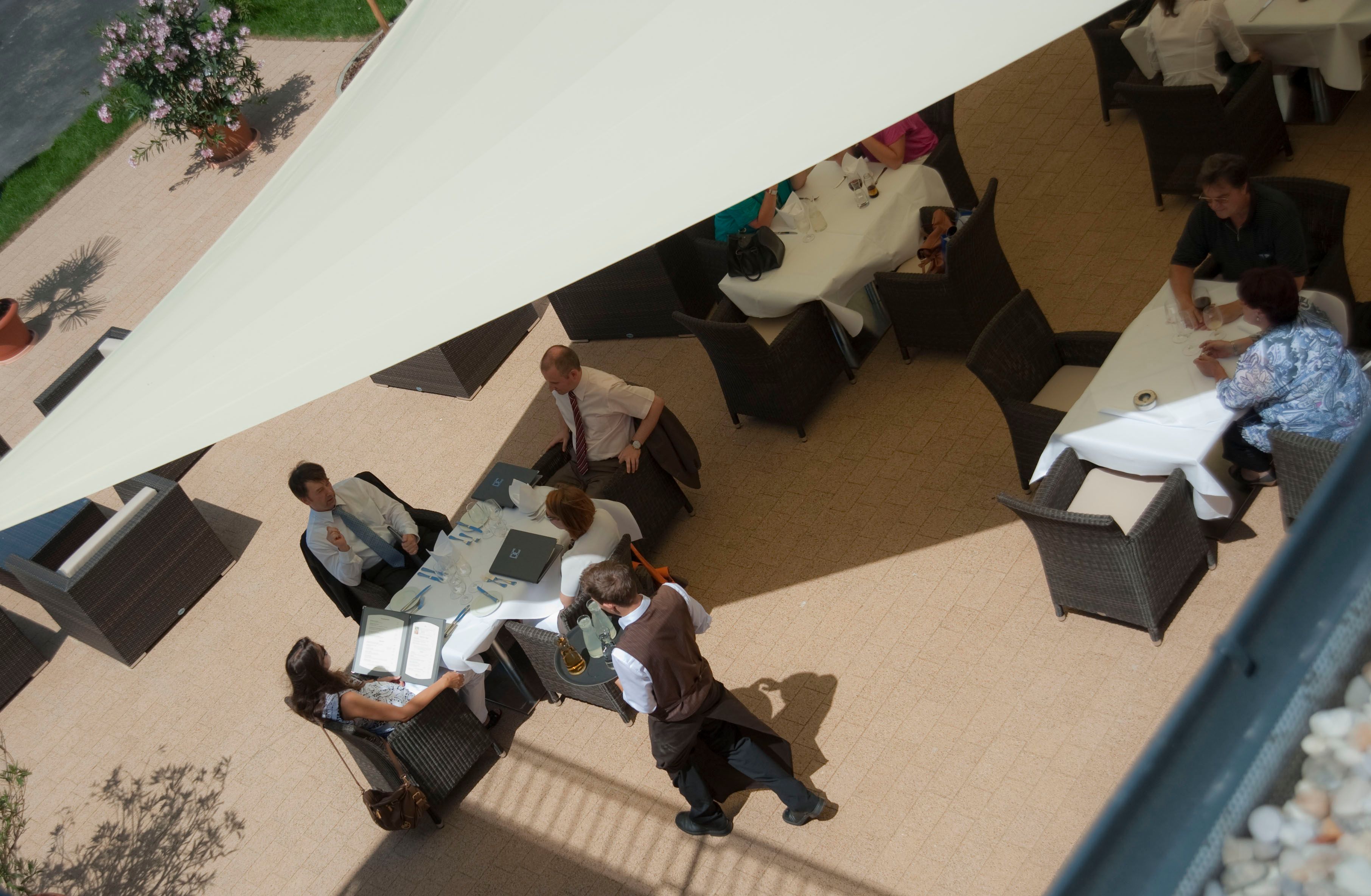 Aerial view of a hotel terrace with guests at tables under an awning.