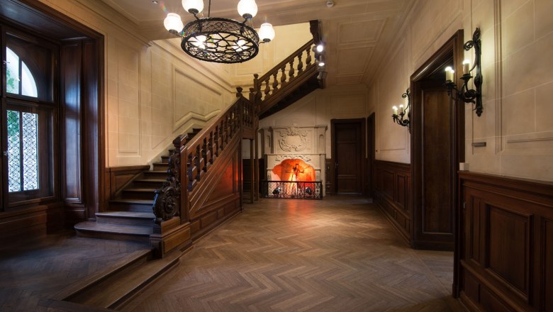 Elegant interior with wooden staircase, fireplace and chandelier in Schloss Rothschild.