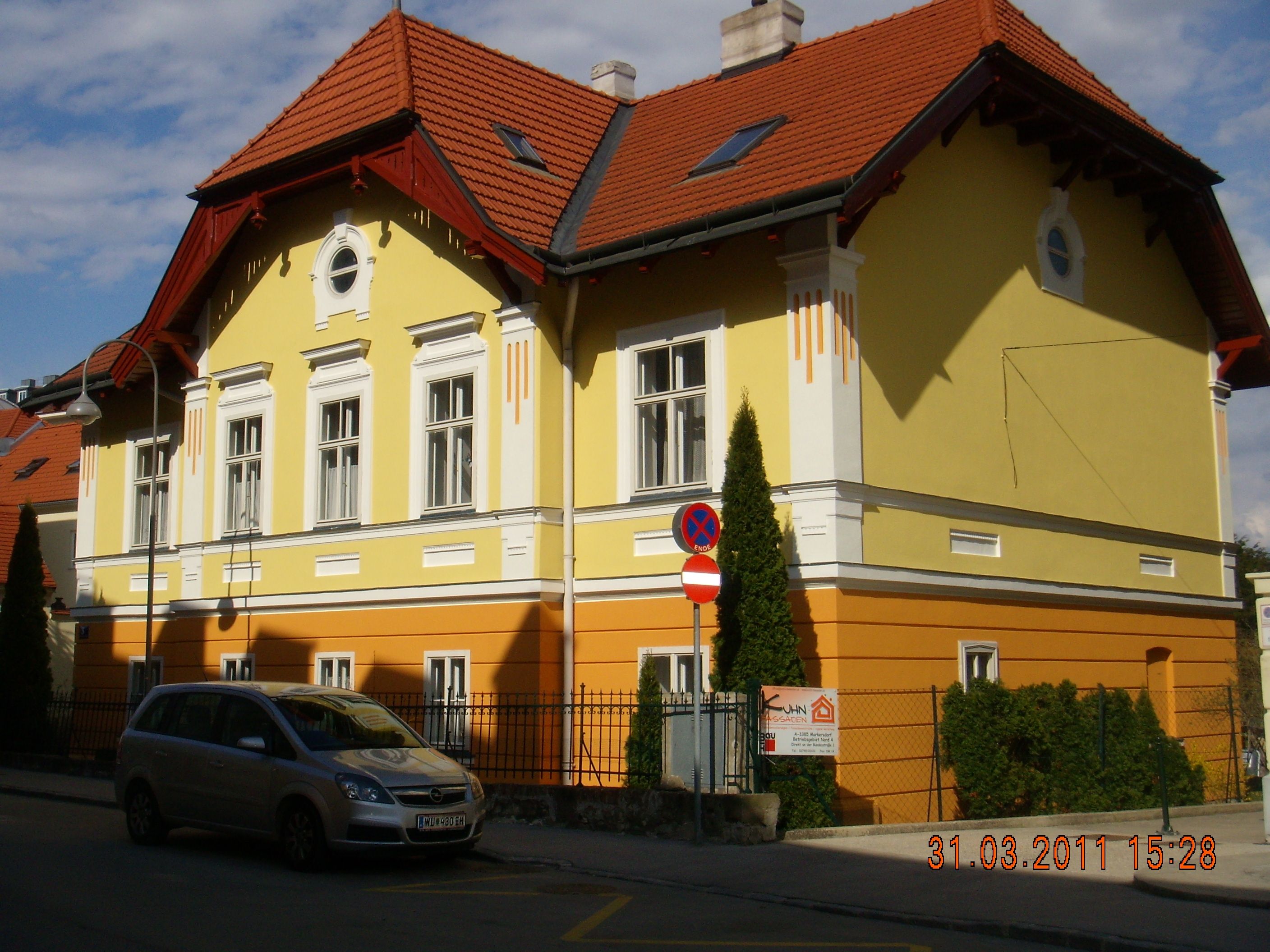 Yellow and orange building with a red roof and a parked car in front of it.