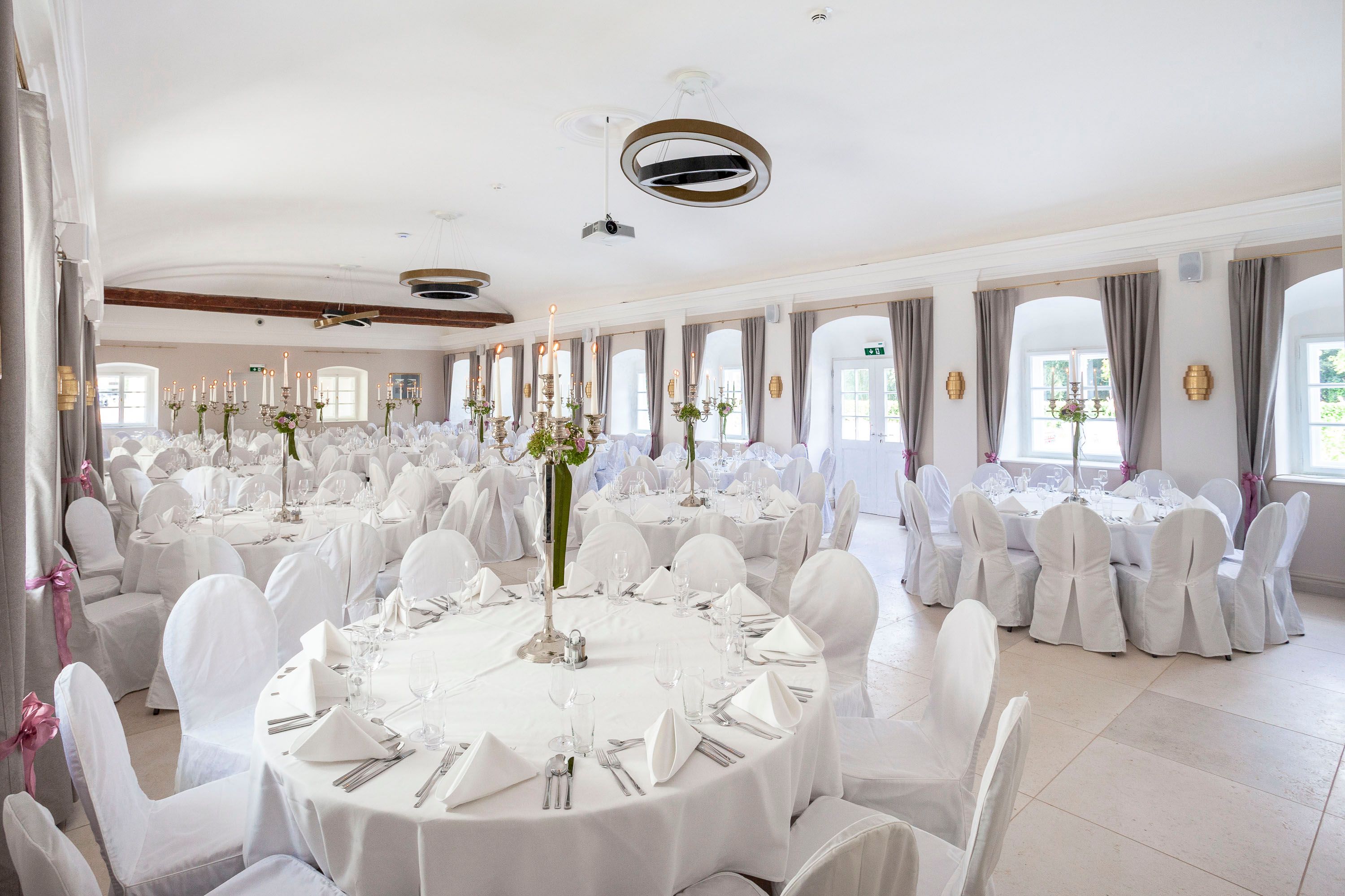 Elegant ballroom with white tables and chairs, decorated with candlesticks and flowers.