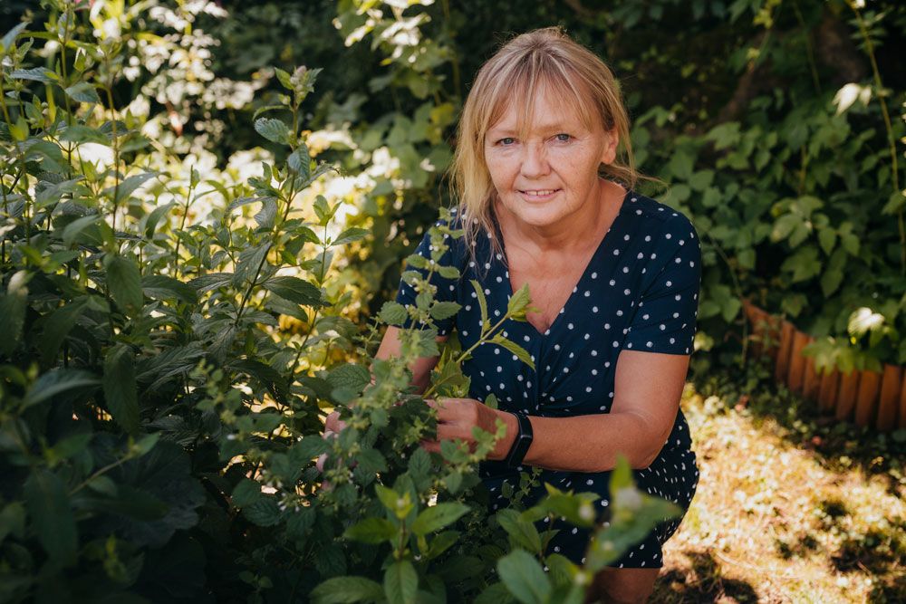 A woman in a polka-dot dress kneels in a garden and looks at plants.