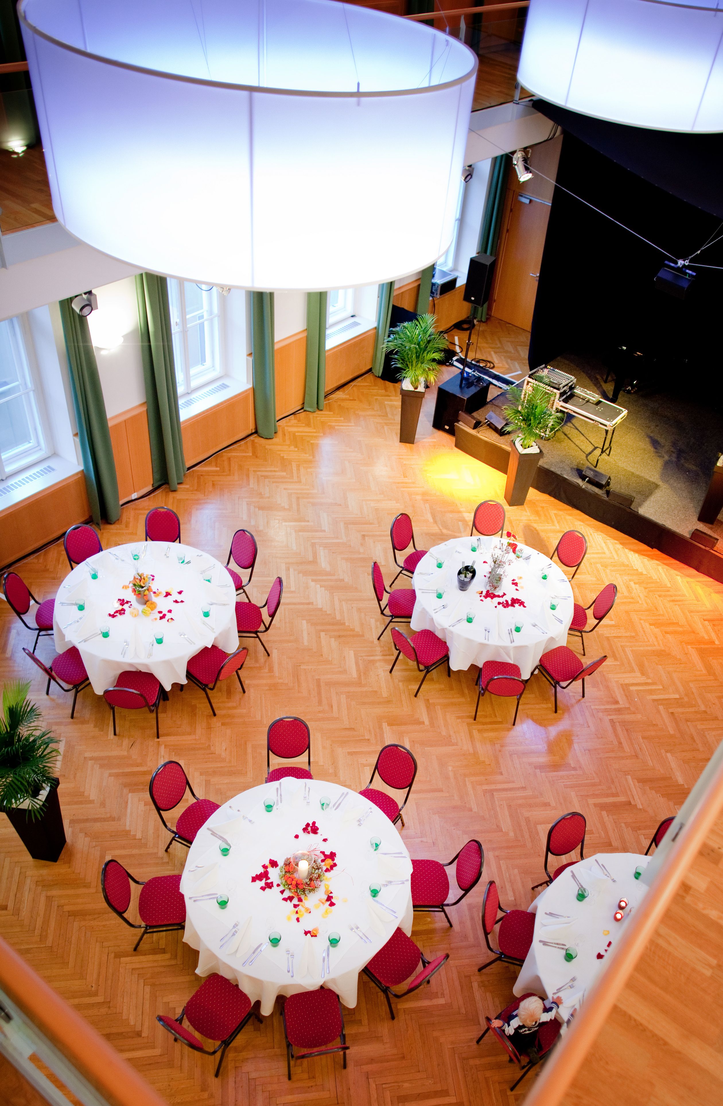A festively decorated hall with round tables and red chairs, view from above.