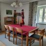 Dining area with wooden table, red table runner, wooden chairs, curtains and decorations on the wall.