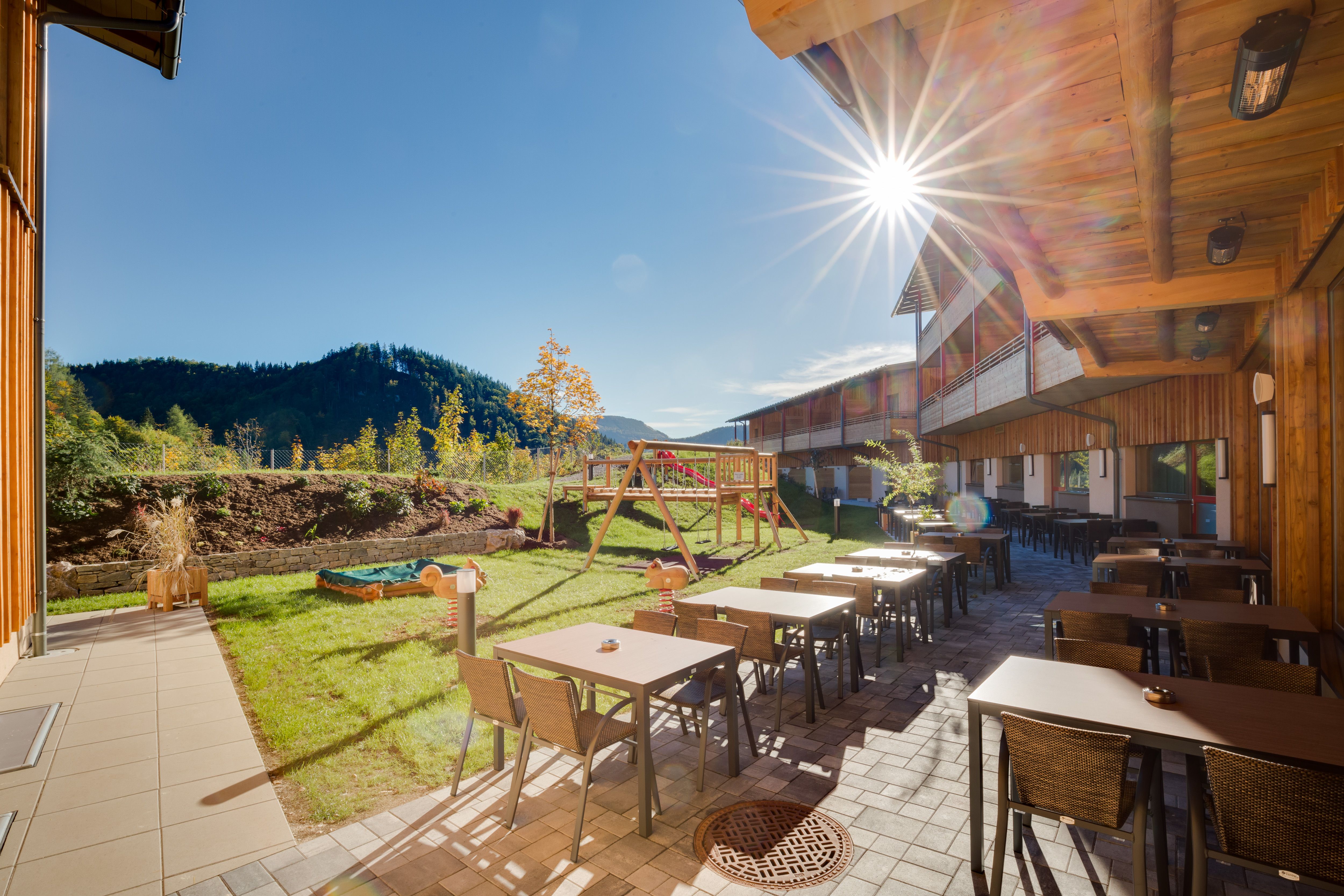 Terrace of the JUFA Hotel Annaberg with tables, chairs and playground in the background in the sunshine.