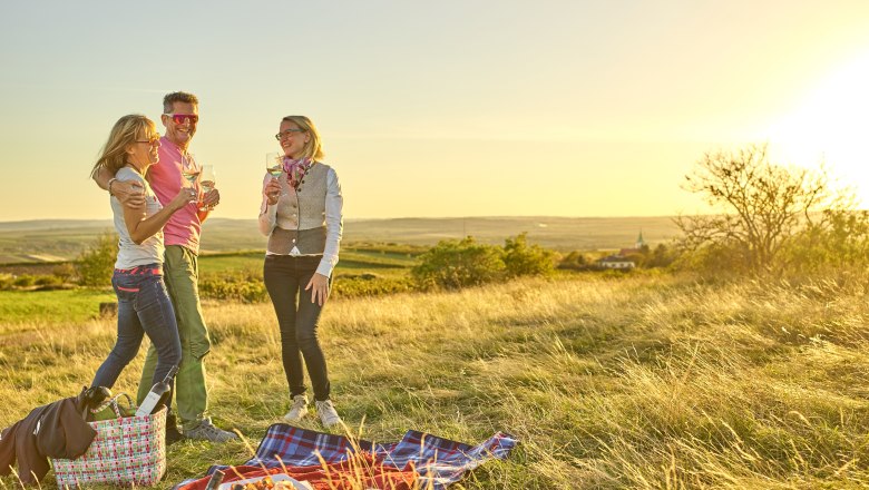 Three people having a picnic in a meadow at sunset.