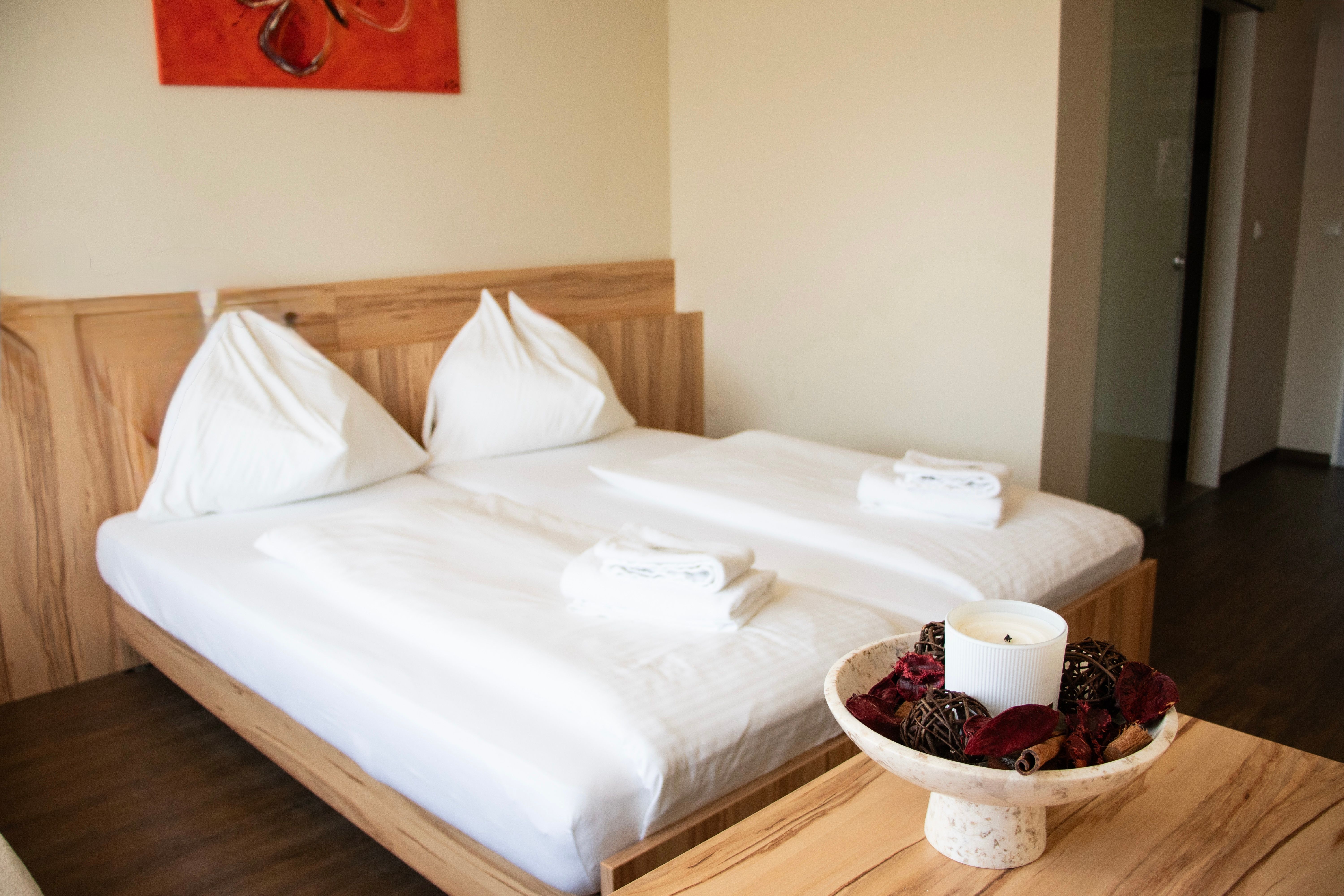 A simple hotel room with a double bed, white towels, and a decorative bowl with a candle on the table.