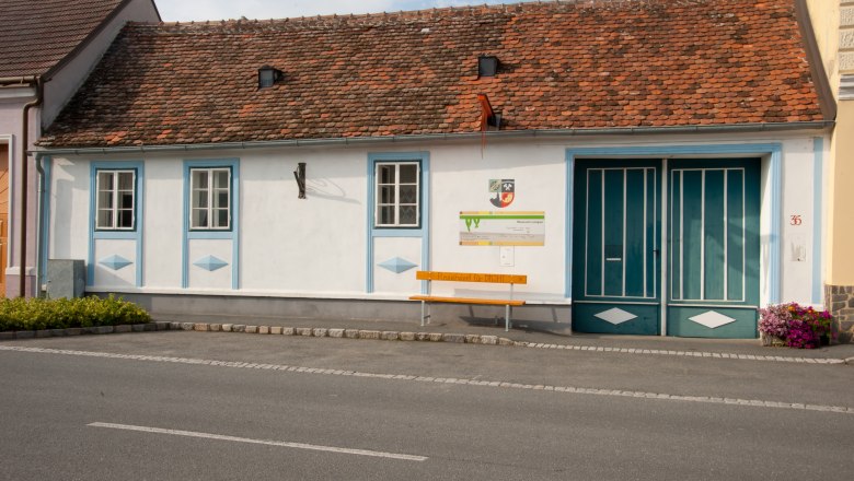 A small, traditional building with red bricks and blue window frames. In front of the building is a yellow bench with the inscription 'Reserved for YOU!