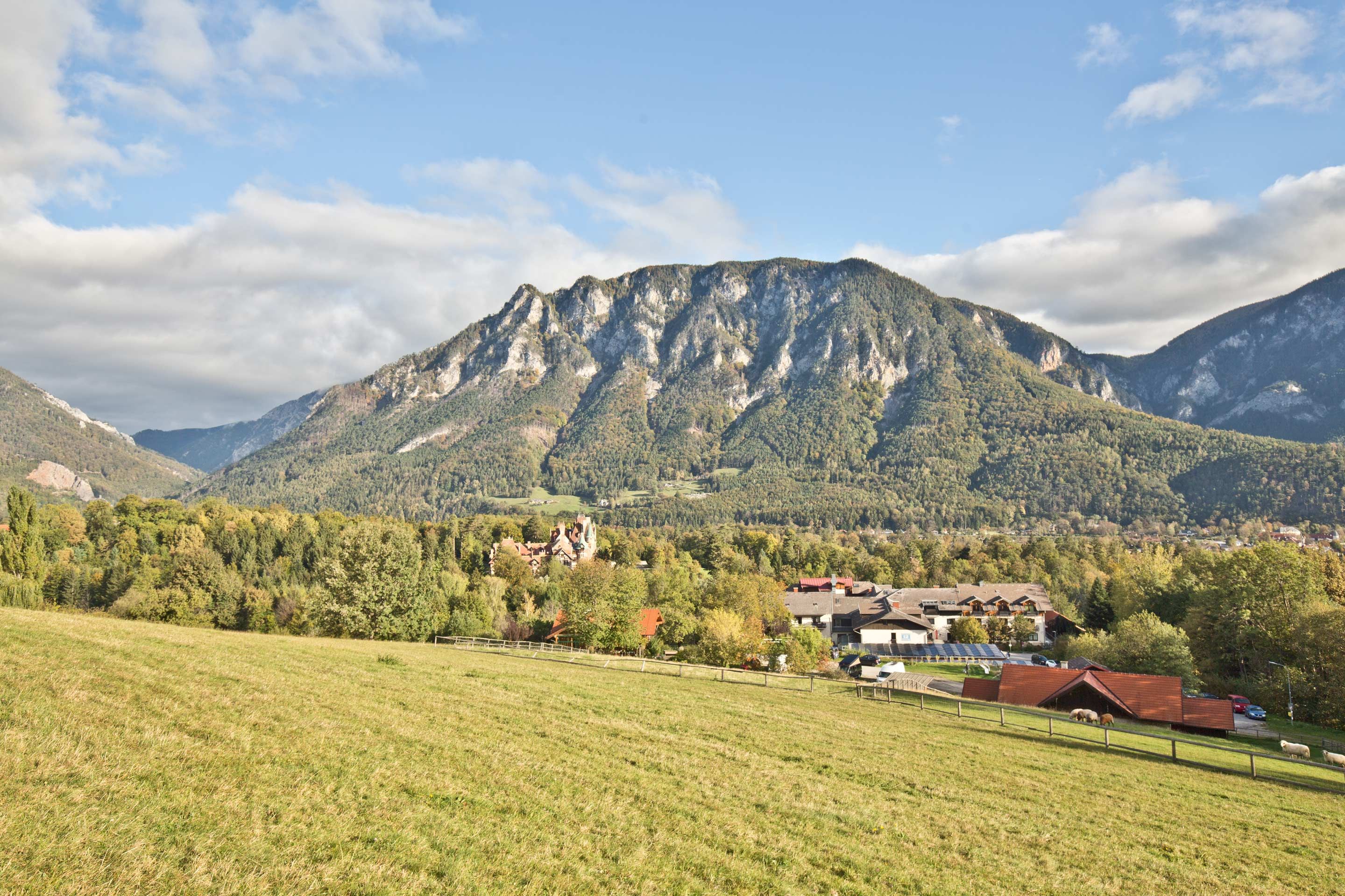 A panoramic view of a mountainous landscape with meadows in the foreground and a village in the background.