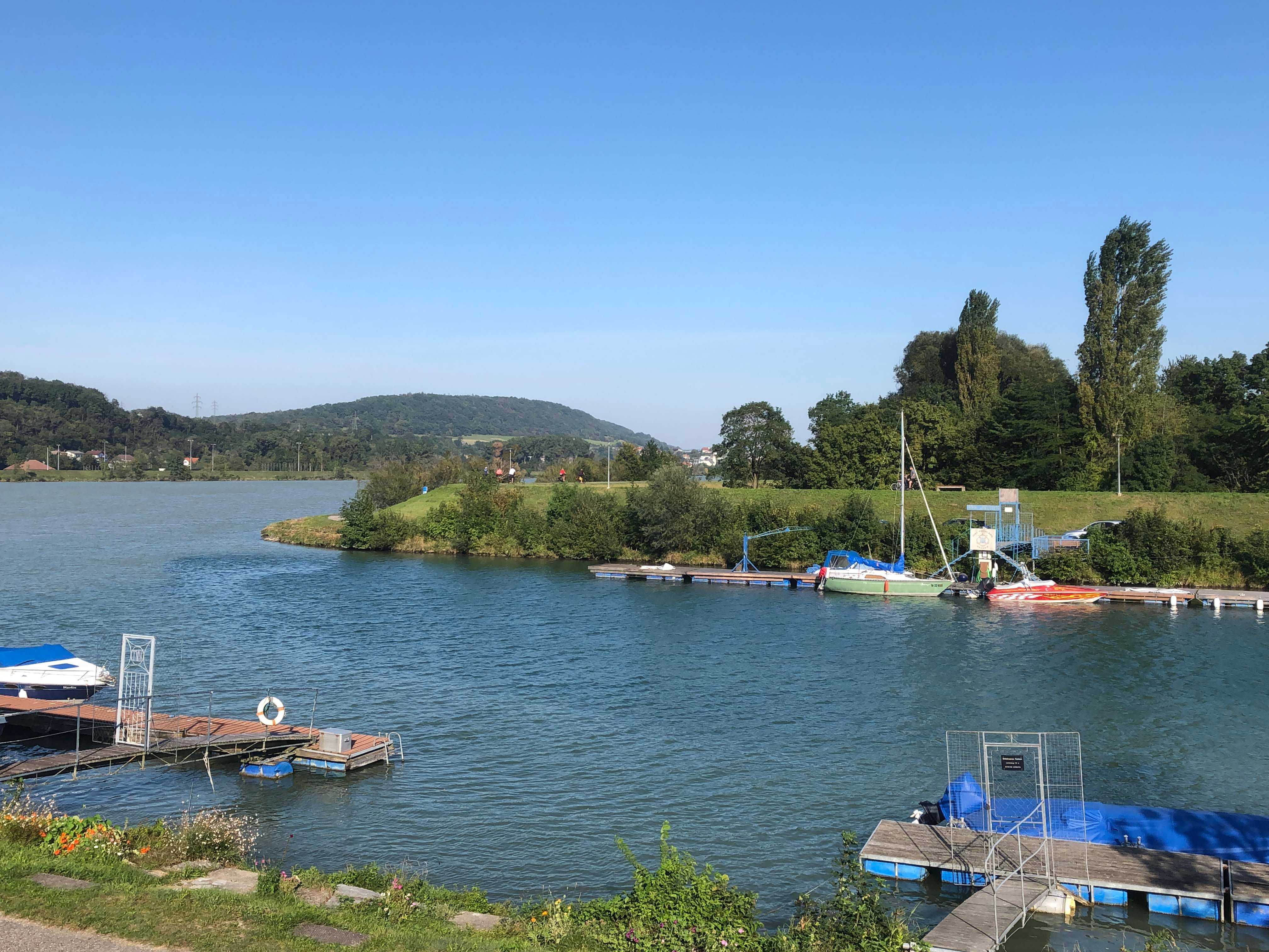 Mooring with boats on the riverbank, surrounded by green landscape and blue sky.