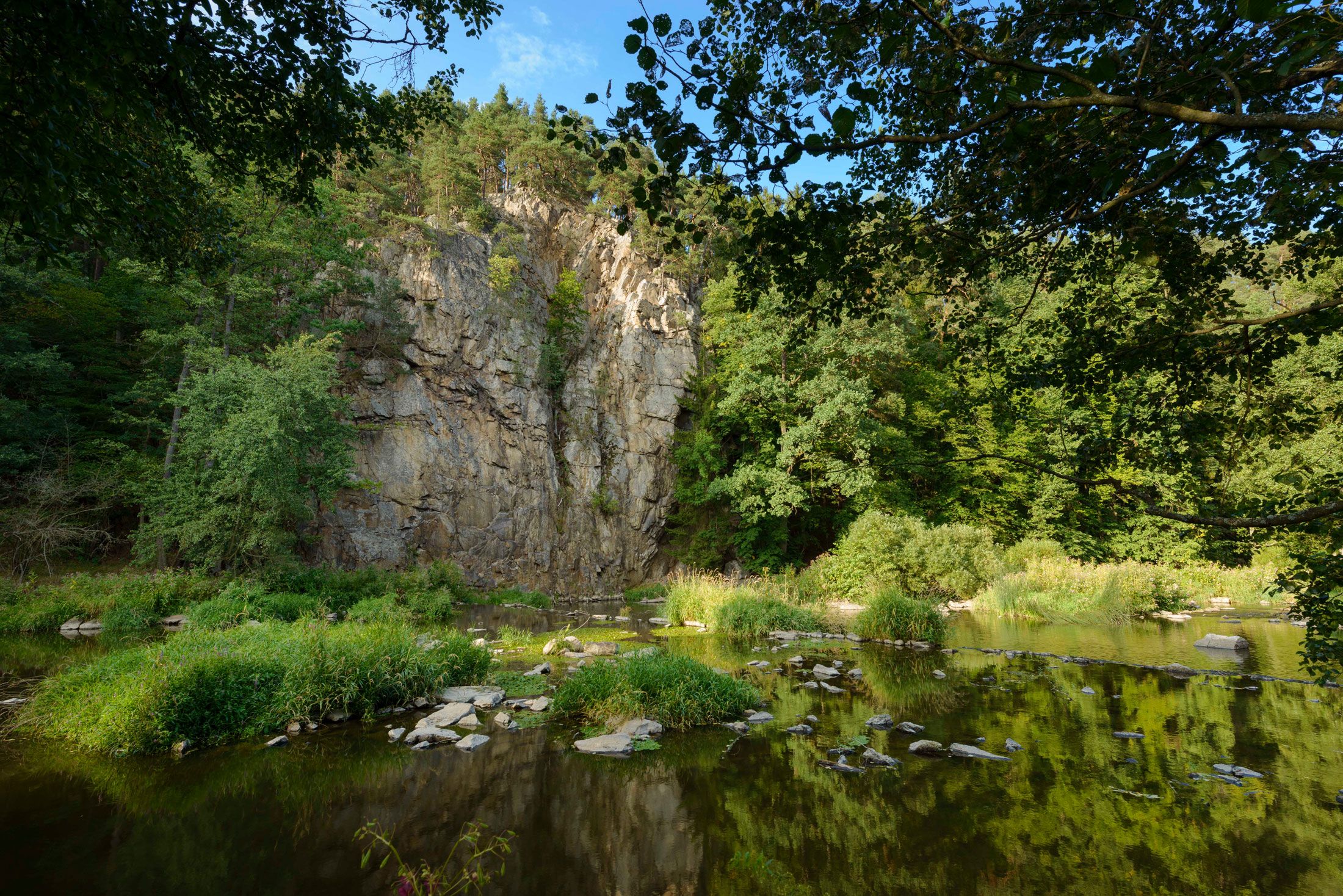 Rock face at the Hahnmühle with trees and river in the foreground.