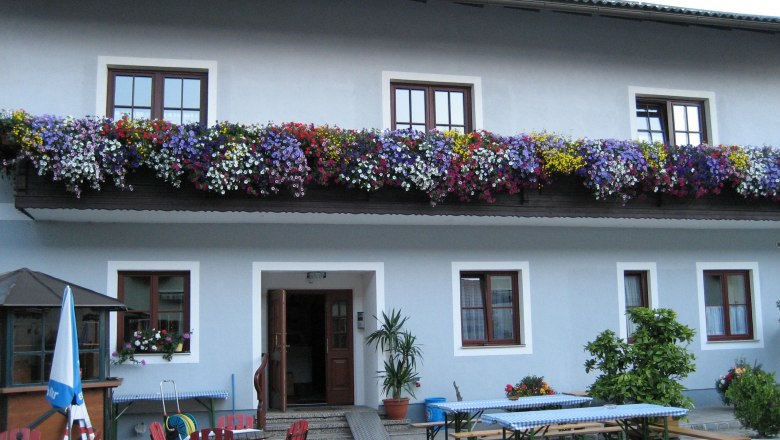 Inn with blue façade, flower boxes on the balcony and beer garden furniture in the foreground.