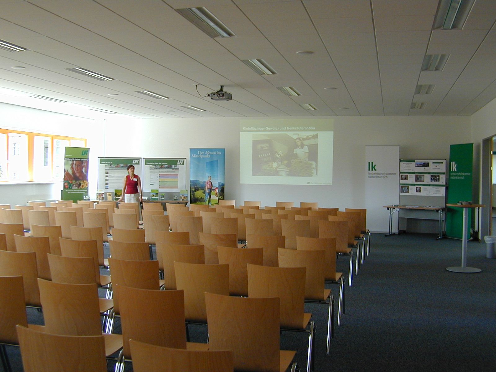 An empty seminar room with wooden chairs, a screen and advertising banners.