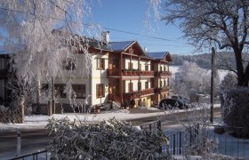 A snow-covered building with wooden balconies and surrounding trees in winter.