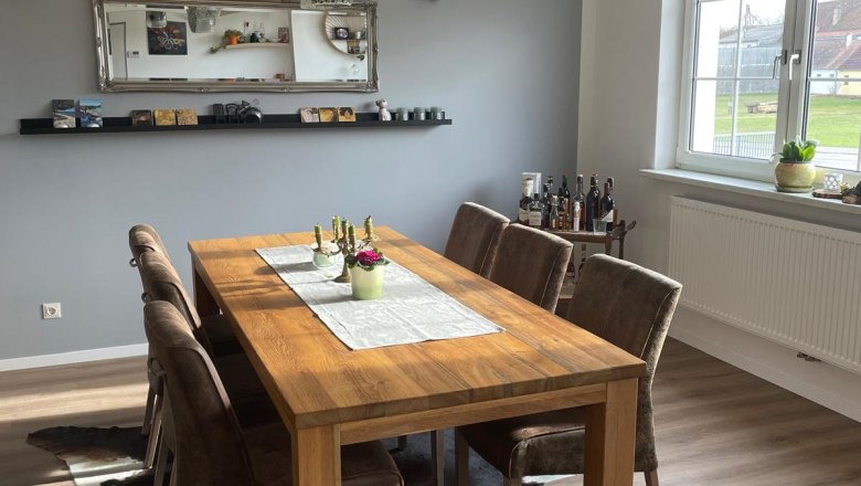 Dining area with wooden table, six chairs, mirror and window.