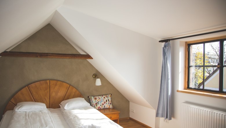 Cozy bedroom with sloping ceiling, double bed, wooden details and window with curtain.