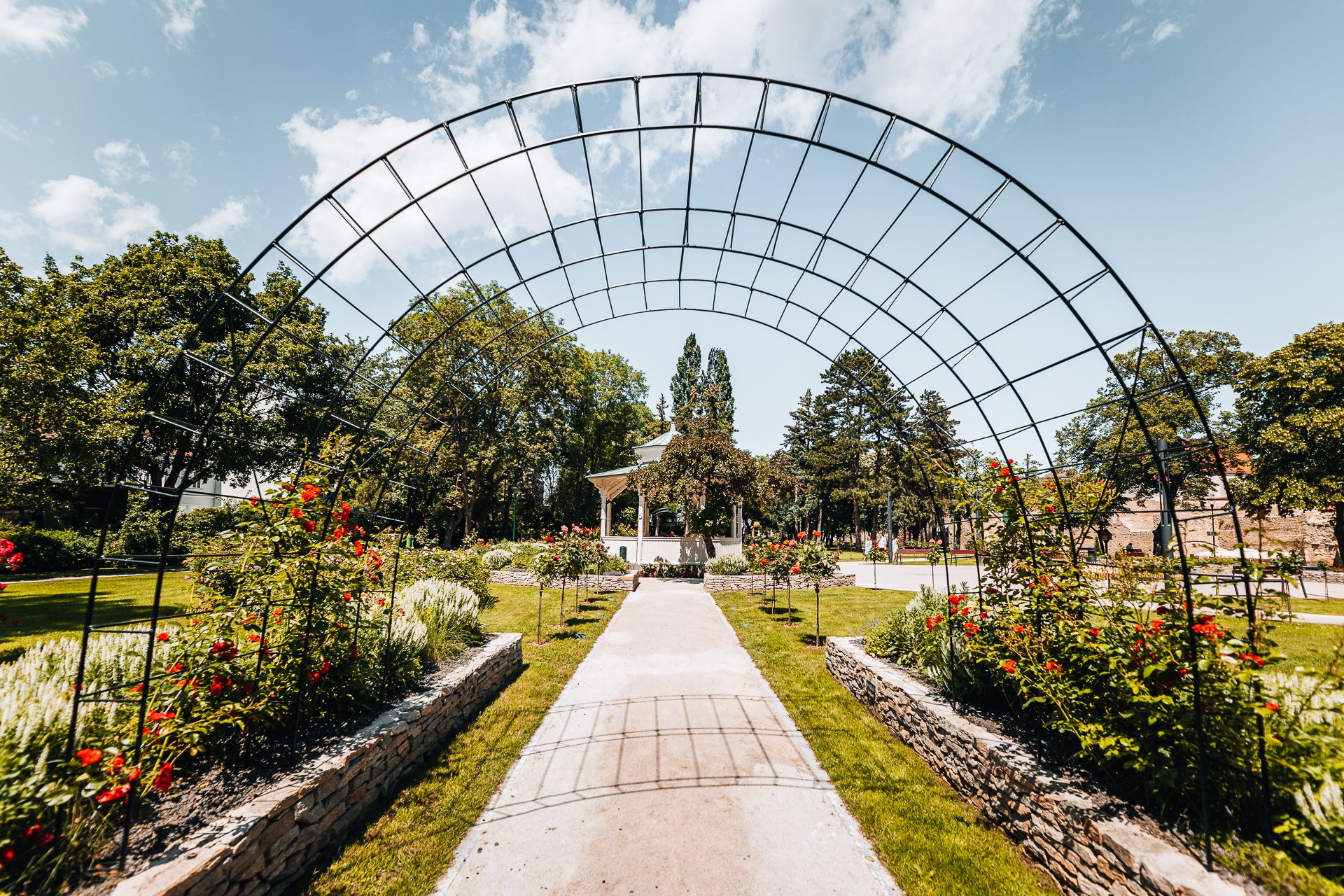 A green city park with a romantic pavilion, a rose garden, and a trellised arch
