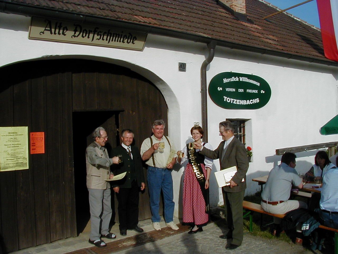 Group of people clinking glasses in front of the old village smithy in Totzenbach.