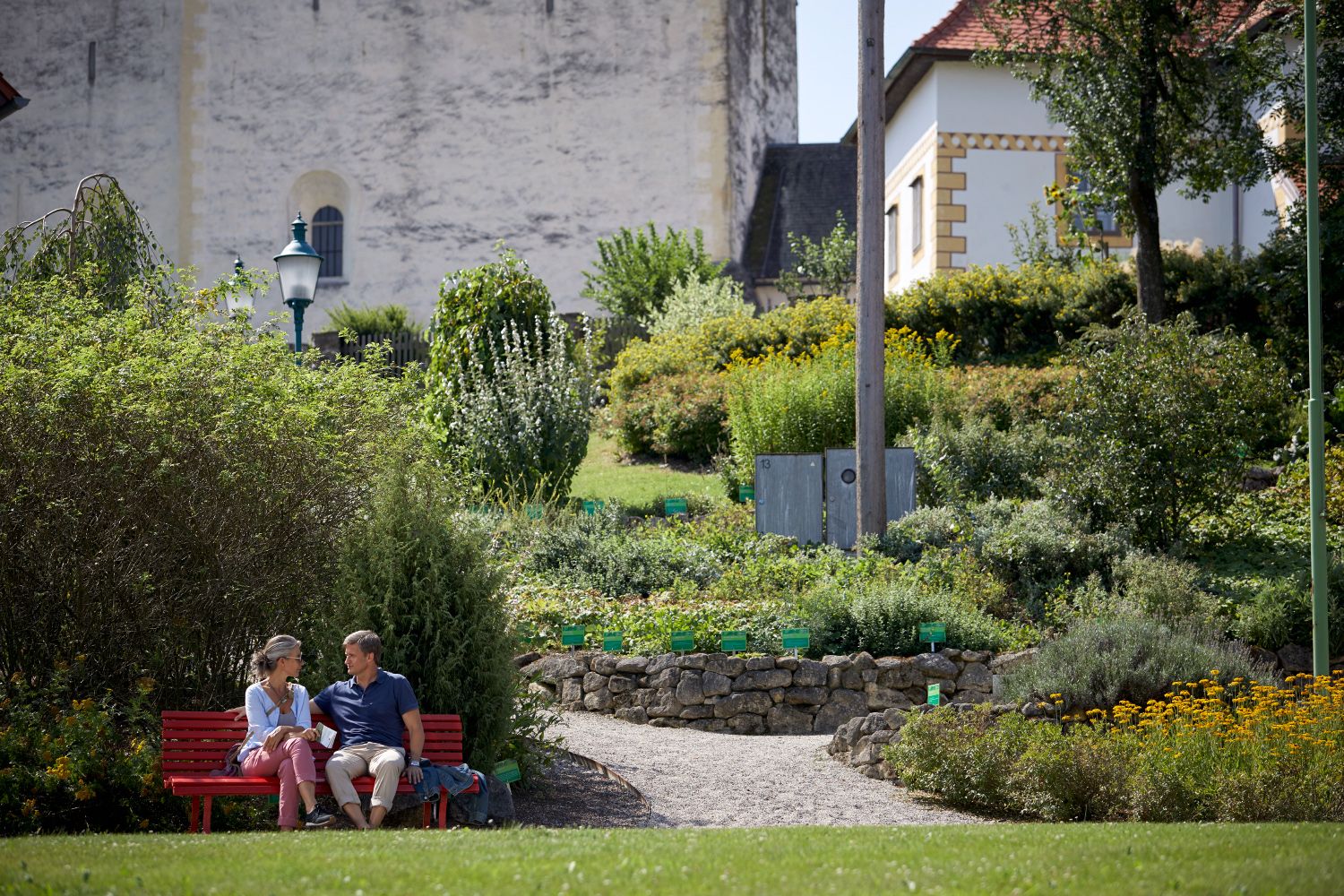 A couple sits on a red bench in a garden in front of the fortified church in Bad Schönau.